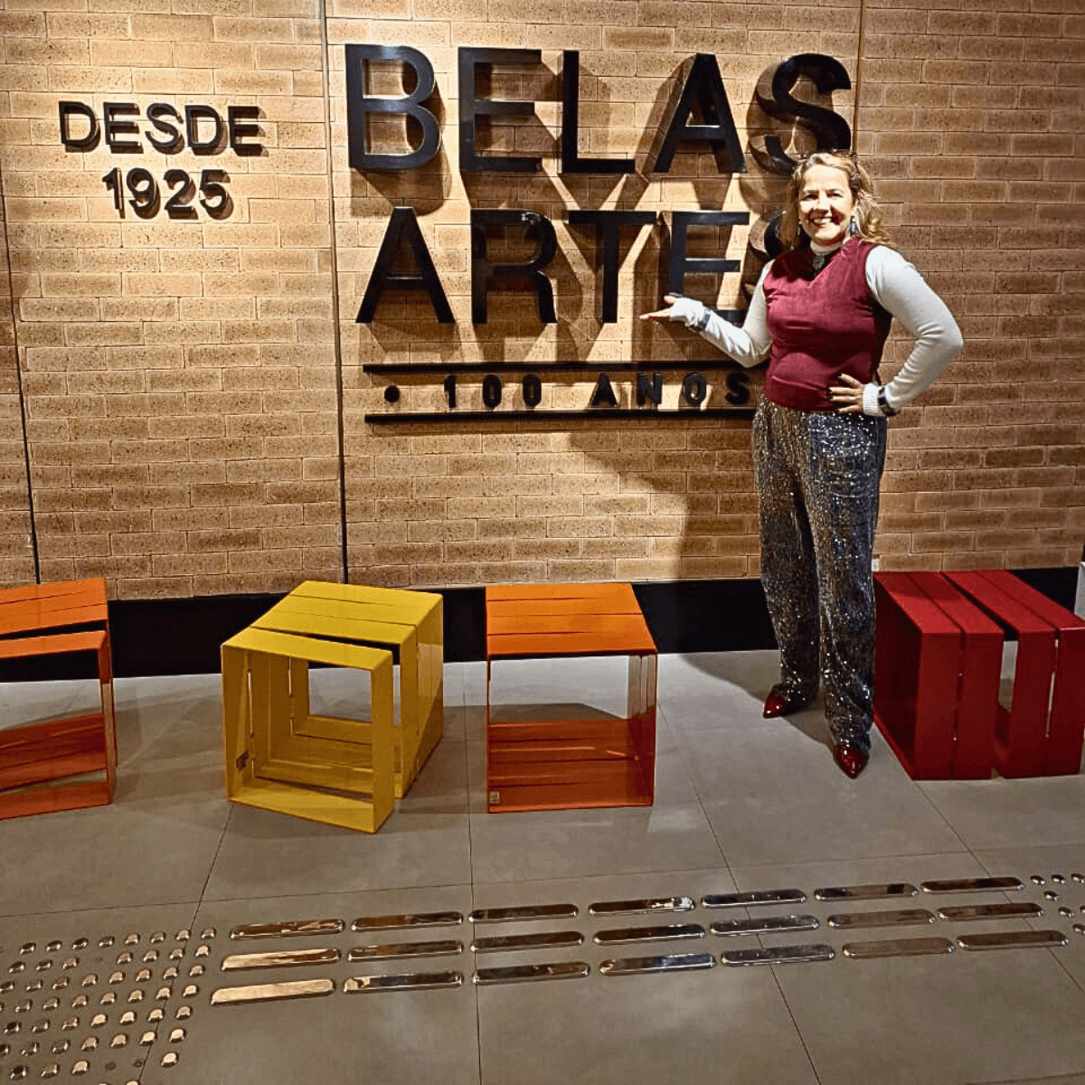 Uma mulher em pé em frente a um letreiro de madeira escrito BELAS ARTES.